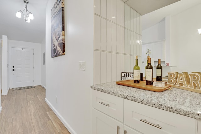 bar with hanging light fixtures, light wood-style flooring, baseboards, and a dry bar