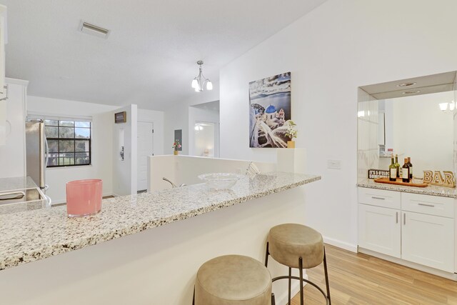 kitchen with visible vents, white cabinets, freestanding refrigerator, light stone countertops, and light wood finished floors