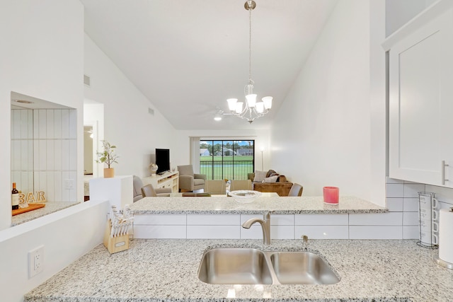 kitchen featuring lofted ceiling, hanging light fixtures, sink, backsplash, and white cabinetry