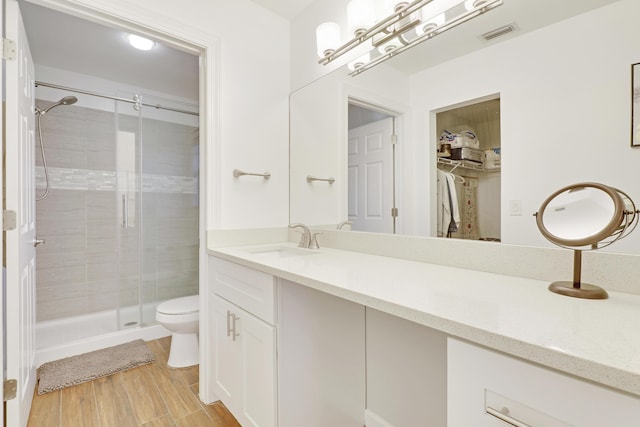 bathroom featuring visible vents, toilet, wood finished floors, vanity, and a shower stall