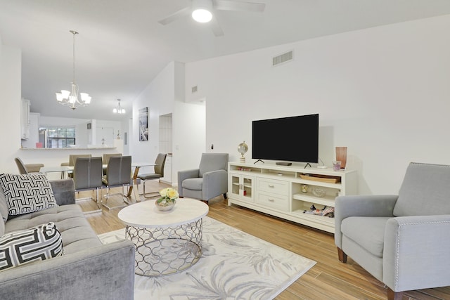 living room with lofted ceiling, ceiling fan with notable chandelier, wood finished floors, and visible vents