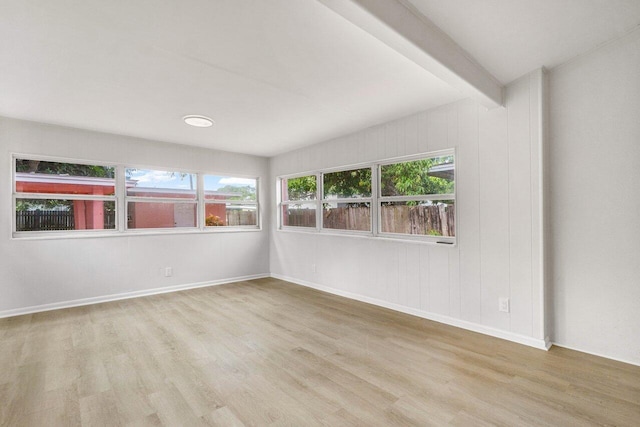 empty room with beamed ceiling, light wood-type flooring, and a wealth of natural light