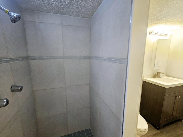 bathroom with tiled shower, a textured ceiling, vanity, and toilet