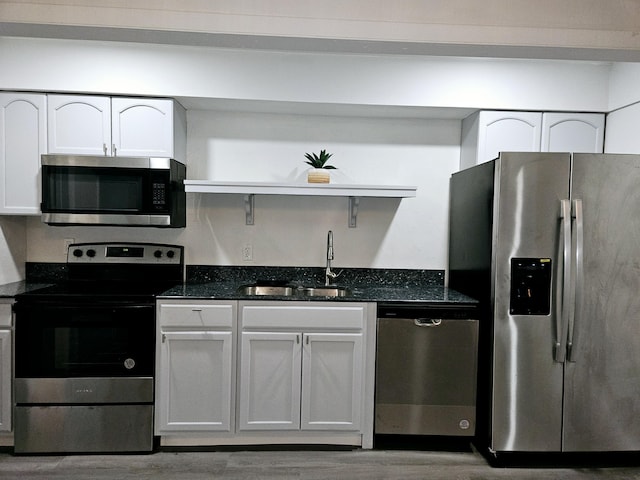 kitchen featuring sink, stainless steel appliances, dark stone countertops, white cabinets, and hardwood / wood-style flooring