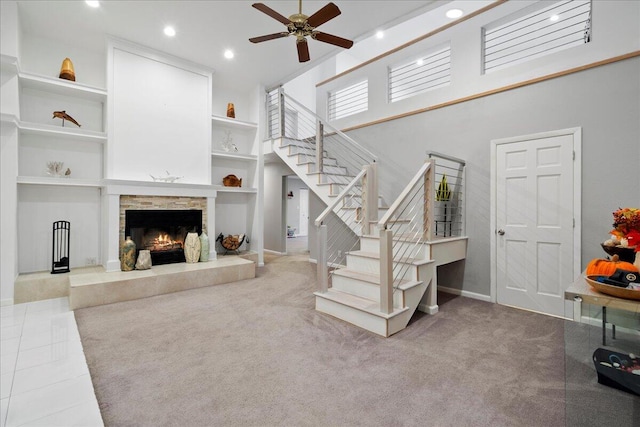 carpeted living room with a stone fireplace, ceiling fan, and a high ceiling