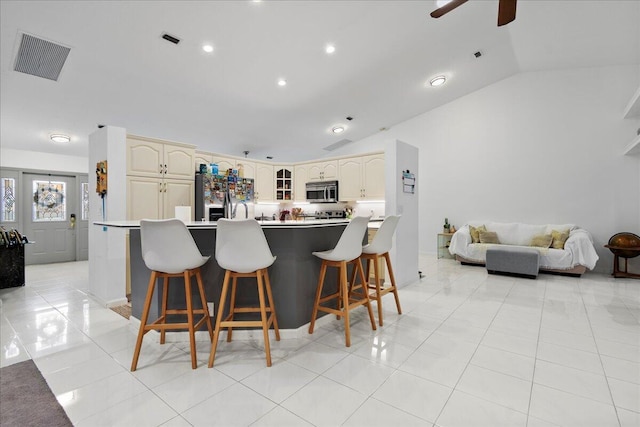 kitchen with a kitchen bar, cream cabinetry, lofted ceiling, and light tile patterned flooring