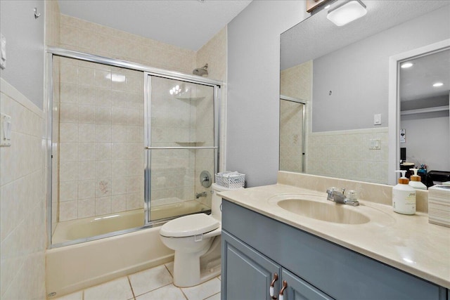 full bathroom with vanity, combined bath / shower with glass door, tile patterned flooring, toilet, and tile walls