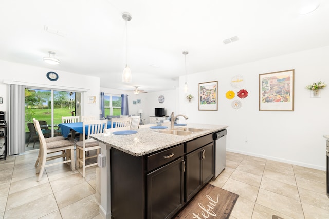 kitchen featuring dishwasher, sink, light stone counters, pendant lighting, and a center island with sink