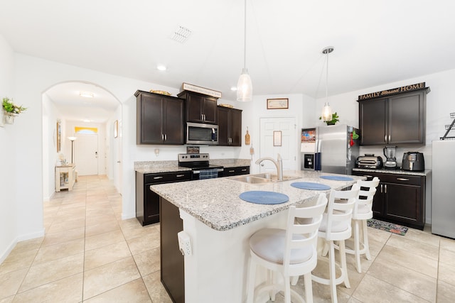 kitchen featuring appliances with stainless steel finishes, dark brown cabinetry, sink, a center island with sink, and decorative light fixtures