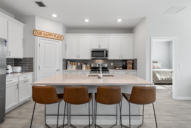 kitchen featuring stainless steel appliances, backsplash, sink, an island with sink, and white cabinets