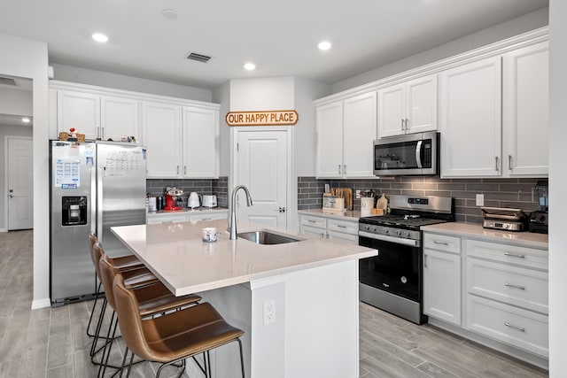 kitchen featuring stainless steel appliances, white cabinetry, sink, an island with sink, and light hardwood / wood-style flooring