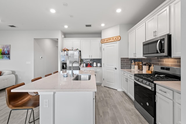 kitchen with stainless steel appliances, light hardwood / wood-style floors, sink, a breakfast bar, and white cabinets