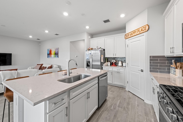 kitchen with white cabinetry, light wood-type flooring, appliances with stainless steel finishes, sink, and a kitchen island with sink