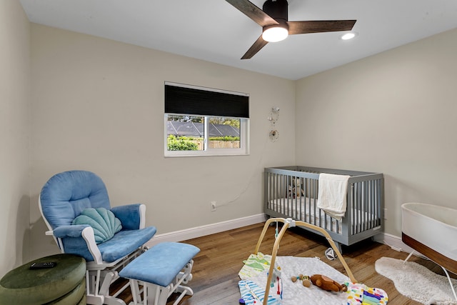 bedroom with hardwood / wood-style floors, ceiling fan, and a crib