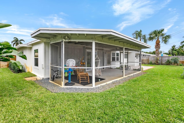 rear view of property featuring a lawn, a sunroom, and a patio area