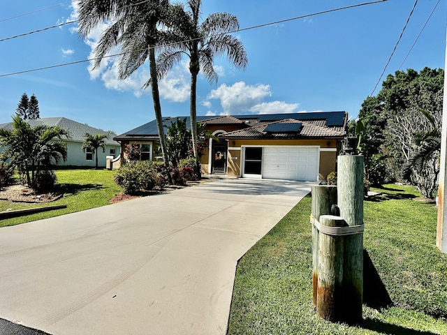 view of front of house with concrete driveway, a tiled roof, an attached garage, roof mounted solar panels, and a front yard