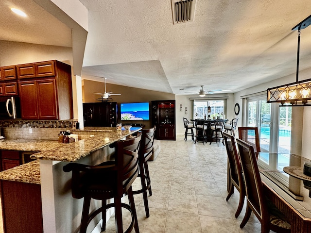 kitchen with lofted ceiling, a peninsula, visible vents, backsplash, and stainless steel microwave