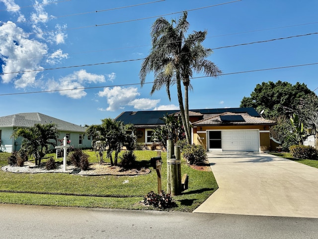 ranch-style house featuring a garage, driveway, a front yard, and roof mounted solar panels