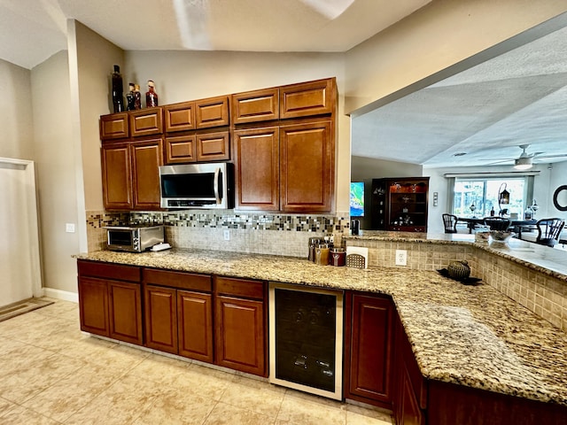 kitchen with beverage cooler, light stone counters, stainless steel microwave, and decorative backsplash