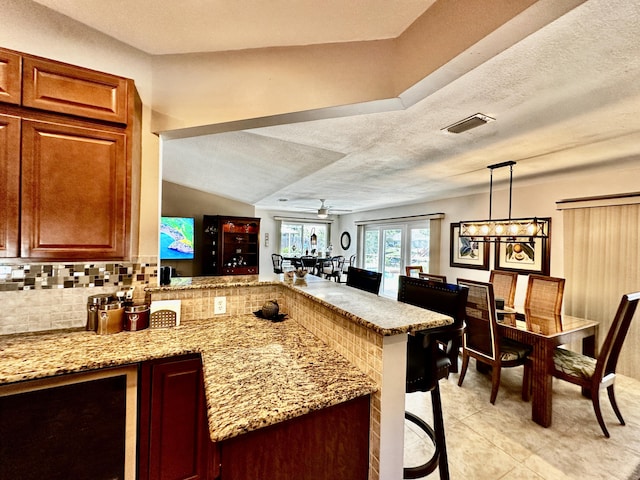 kitchen featuring a peninsula, decorative backsplash, visible vents, and light stone countertops