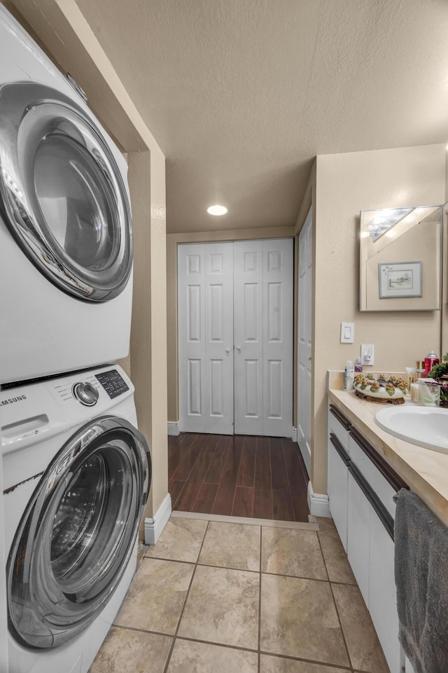 laundry room featuring stacked washer / drying machine, sink, a textured ceiling, and light hardwood / wood-style flooring