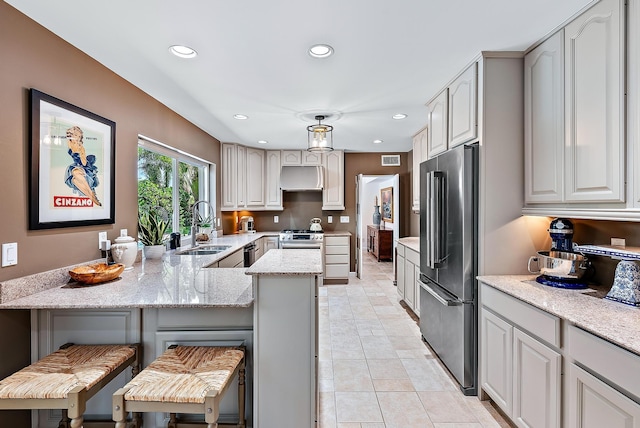 kitchen featuring a breakfast bar, sink, light stone countertops, appliances with stainless steel finishes, and kitchen peninsula