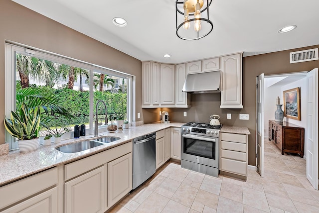 kitchen with ventilation hood, sink, light stone counters, and appliances with stainless steel finishes