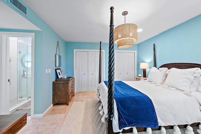 tiled bedroom featuring a chandelier, two closets, and ensuite bath