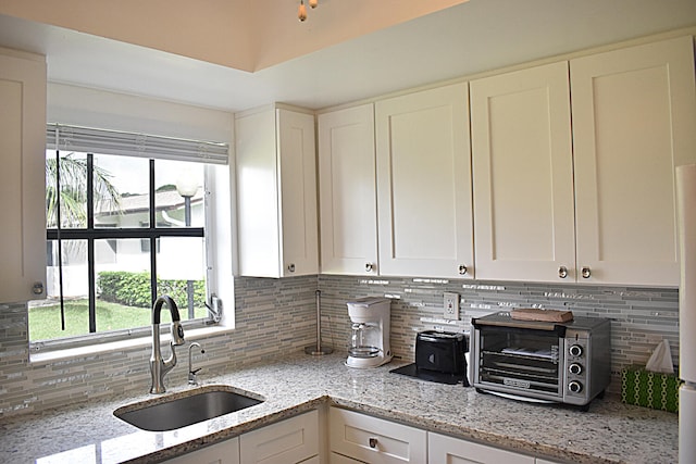 kitchen with white cabinetry, tasteful backsplash, sink, and light stone counters