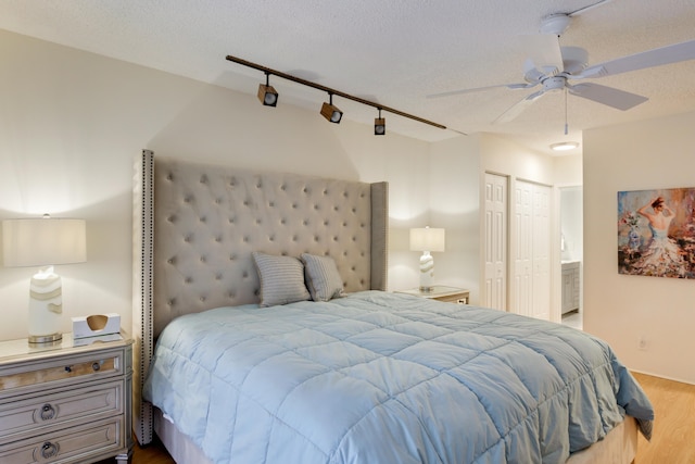 bedroom with a textured ceiling, hardwood / wood-style flooring, rail lighting, two closets, and ceiling fan