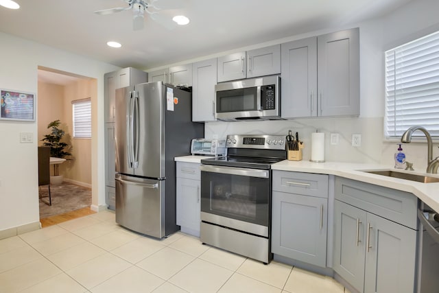 kitchen featuring stainless steel appliances, sink, ceiling fan, light tile patterned floors, and gray cabinetry