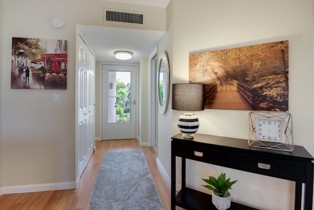 doorway to outside featuring a textured ceiling and light hardwood / wood-style floors