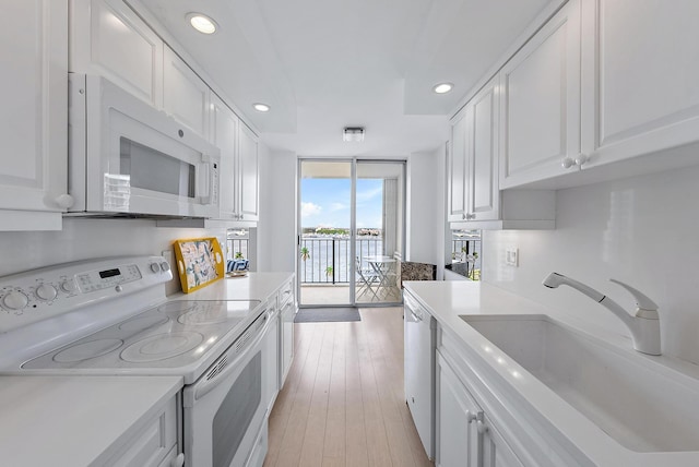 kitchen with white appliances, white cabinetry, light countertops, and a sink