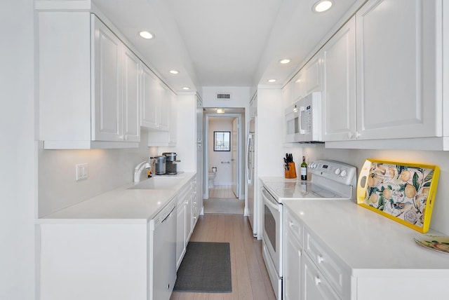 kitchen with white appliances, light countertops, a sink, and white cabinetry