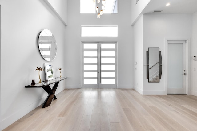 foyer entrance with light wood-type flooring, french doors, and a towering ceiling