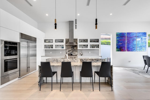 kitchen with pendant lighting, white cabinetry, wall chimney range hood, and appliances with stainless steel finishes