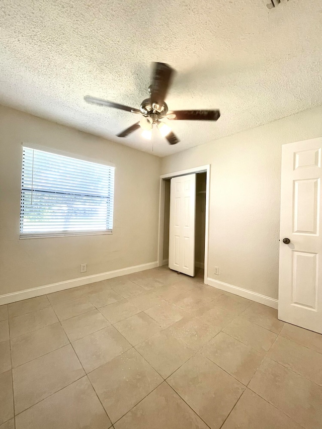 unfurnished bedroom featuring a textured ceiling, a closet, ceiling fan, and light tile patterned flooring