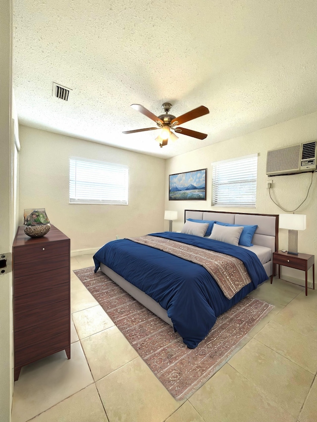 bedroom with a wall unit AC, ceiling fan, light tile patterned flooring, and a textured ceiling