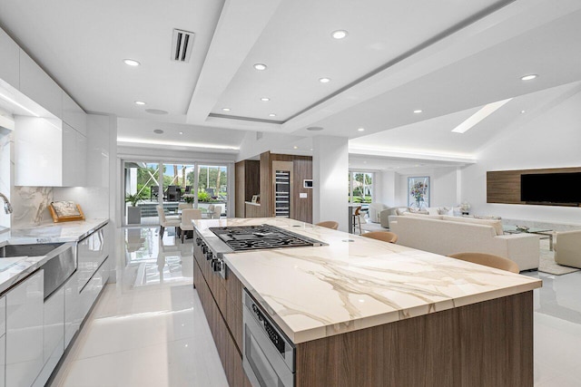 kitchen featuring light stone counters, light tile patterned flooring, stainless steel appliances, white cabinetry, and a large island