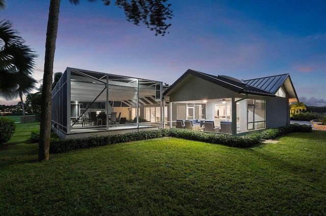 back house at dusk with a patio area and a lawn