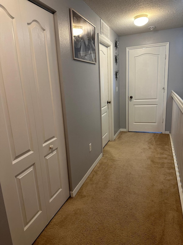 hall featuring light colored carpet and a textured ceiling