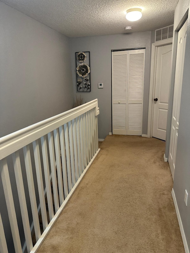 hallway with light carpet and a textured ceiling