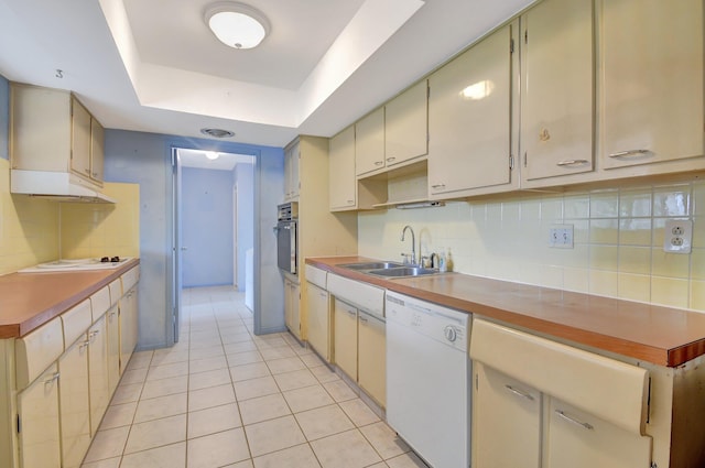 kitchen with white appliances, a tray ceiling, sink, light tile patterned floors, and cream cabinetry