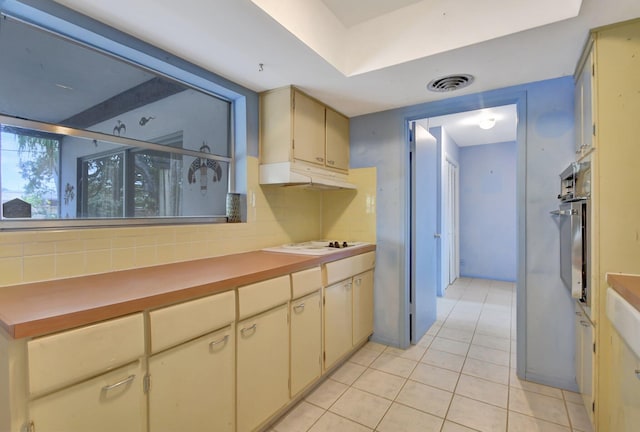 kitchen featuring stainless steel oven, tasteful backsplash, cream cabinets, white cooktop, and light tile patterned floors