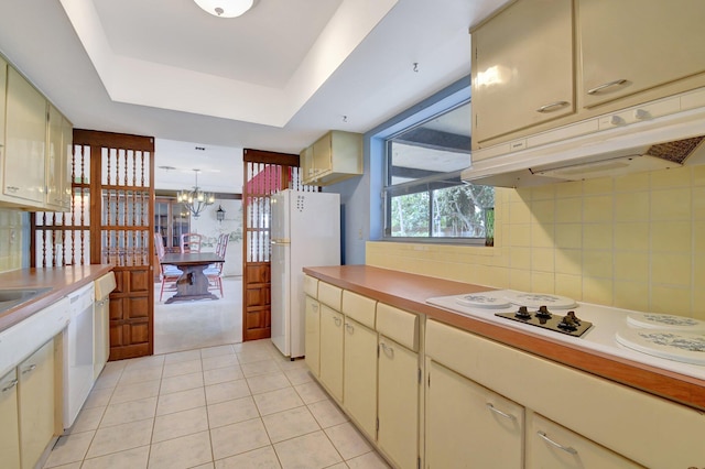 kitchen with cream cabinets, white appliances, a raised ceiling, and light tile patterned flooring