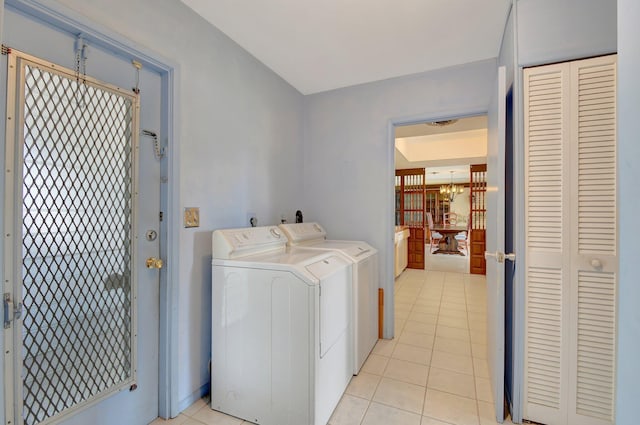 clothes washing area with light tile patterned flooring, washing machine and dryer, and a chandelier