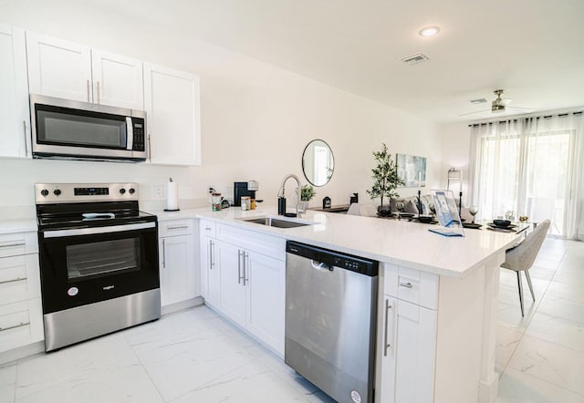 kitchen featuring appliances with stainless steel finishes, sink, white cabinets, kitchen peninsula, and ceiling fan