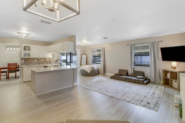 kitchen featuring backsplash, white cabinets, sink, light wood-type flooring, and a chandelier