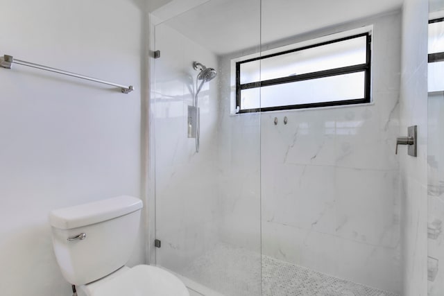 bathroom featuring a shower with door and toilet