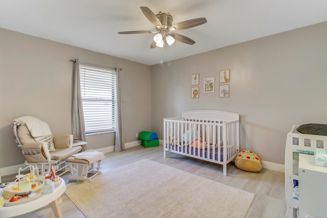 bedroom featuring light wood-type flooring, a nursery area, and ceiling fan